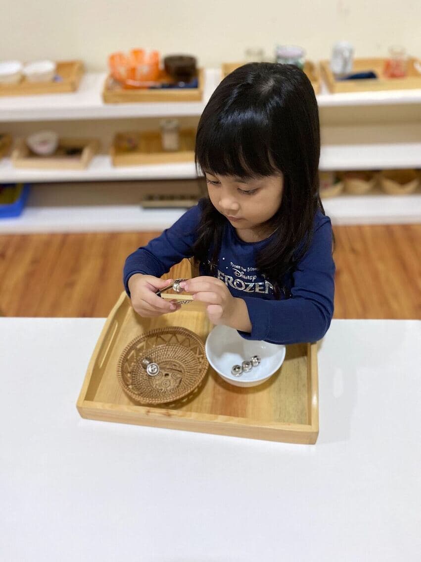 A child practicing a transferring exercise with a spoon and small objects