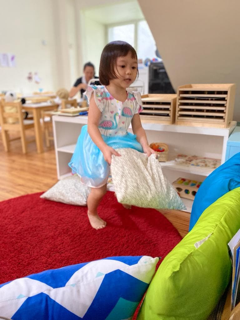 A child carrying a cushion in a cozy classroom reading corner